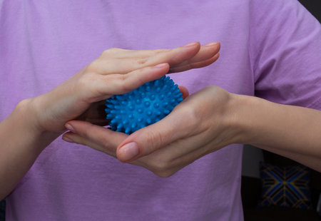 Woman holding blue textured massage ball in hands for stress relief and hand therapyの写真素材