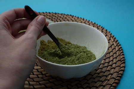 Hand mixing natural henna powder with spoon in bowl preparing herbal hair dyeの写真素材