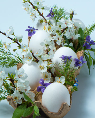 Easter decor on a light blue background. White chicken eggs in a cardboard box with spring flowers. Festive spring postcard. High quality vertical photoの写真素材