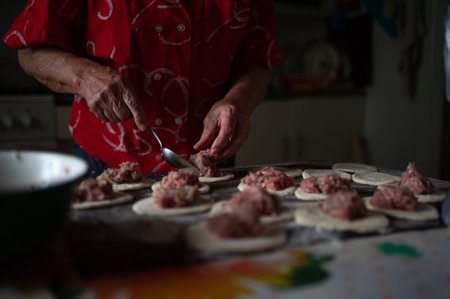 Old female hands at work in the kitchen close up. Grandmother puts meat on the dough with iron spoon. The process of making traditional meat pies. High quality dark photoの写真素材