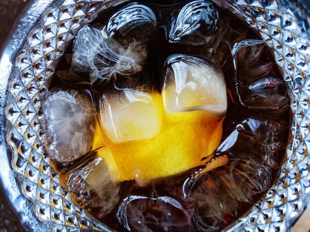 Pieces of ice and lemon float in a glass with a dark carbonated drink. Close-up. view from above .の写真素材