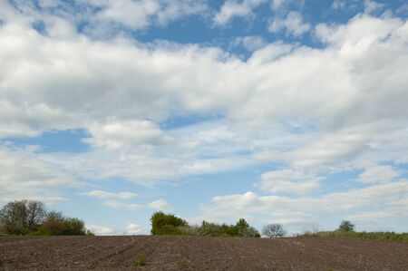 Plowed field in spring against the blue sky and white cloudsの写真素材