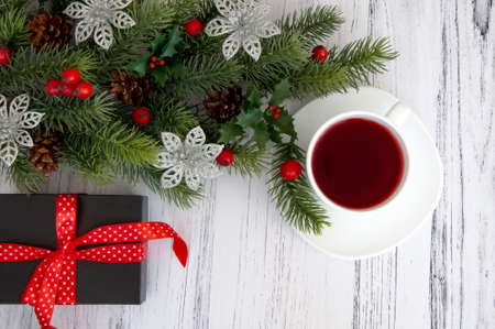 Decorated branches of a Christmas tree, cones, red berries, gifts and a cup of tea on a wooden table. Christmas decor.の写真素材