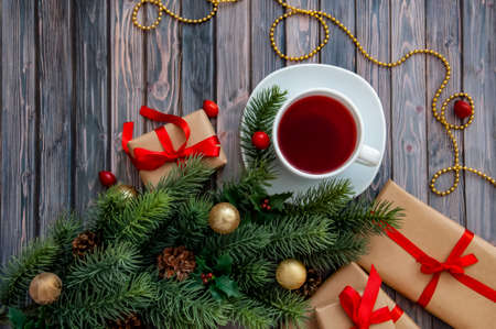 Decorated branches of a Christmas tree, cones, red berries, gifts and a cup of tea on a wooden table. Christmas decor.の写真素材