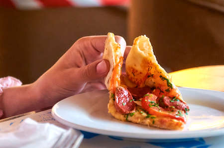 Girl's hand holding a slice of pizza over a plate