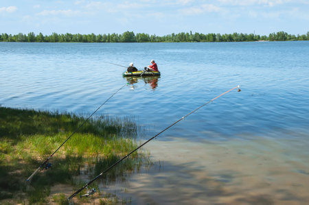 Men on an inflatable boat in the river fishing with fishing rodsの写真素材
