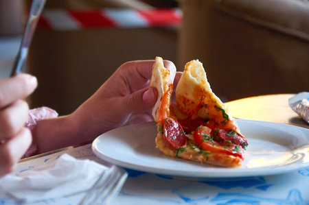 Hand holding a slice of Pizza with sausage, tomato and cheese close-up. Delicious foodの写真素材