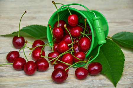 Red cherries in a small green bucket on a wooden backgroundの写真素材