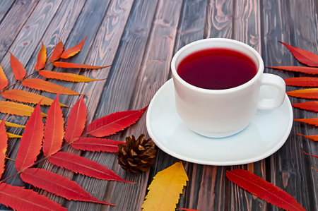 White cup of natural tea with rose hips on a wooden background with autumn leaves. Autumn lifestyleの写真素材