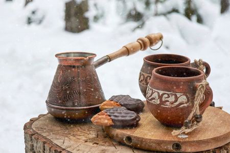 Turk and clay cups with coffee on a wooden stump in a snowy winter forestの写真素材
