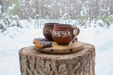 Clay cups with coffee and cookies on a wooden stump in a snowy winter forestの写真素材