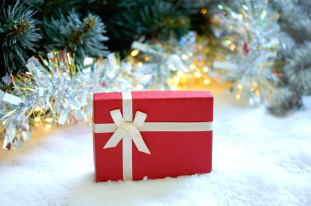 Christmas composition with fir tree branches, red gift box and silver tinsel in golden light of garlandの写真素材