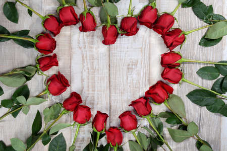 elebration of valentines day, congratulations to lovers. Heart shape lined with red roses on a light wooden texture background. Love symbol. Heart frame made of flowers with place for text.の写真素材