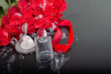 Bottle of mens and perfume and wooden hearts with red roses on a mirrored dark background with water drops. Presentation of male perfume. Gift for a man on valentines dayの写真素材
