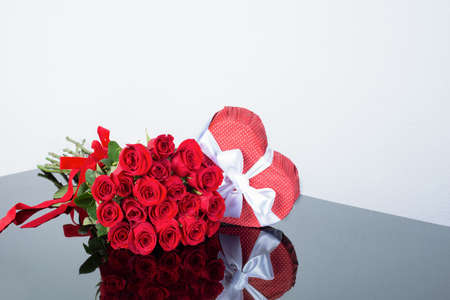 Shaped heart gift box and bouquet red classic roses on a mirror surface. Festive floristry. Gift to a woman. Sample greeting card, invitation for a holiday, declaration of love. Happy valentines dayの写真素材