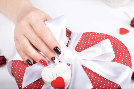 Hands with Fashionable Gel Manicure Open Gift Box with bow. Beautiful Nails and decorative hearts. Woman hand close up. Decorative manicureの写真素材