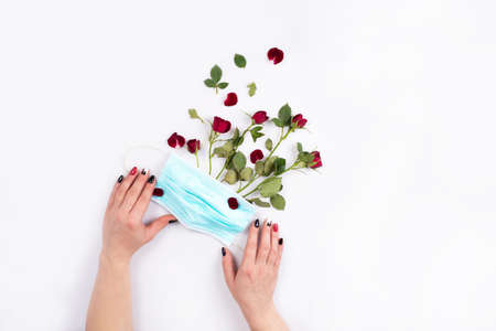 female hands holding a medical mask with a bouquet of roses. New reality ,life in a pandemiaの写真素材