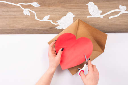 Hands cut out with scissors a paper heart. Kraft paper envelope. love letter preparation for valentine's day. a letter from a lover.Making a gift from paper.DIY products, hand madeの写真素材