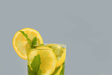 sliced lemon circles and sprigs of mint in water in a transparent glass on a gray background. Lemon mint drink. Vitamin drink, chilled cocktailの写真素材