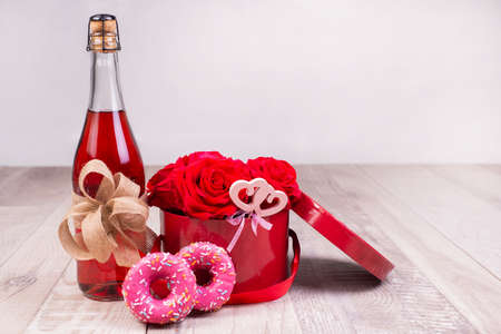 Bottle of champagne, box with red roses ,rustic ribbon, donuts on a wooden surface. Festive congratulations background. Greeting card..の写真素材