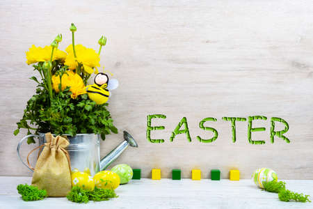 Yellow ranunculus buttercups in a metal watering can, decorative bee, Easter painted eggs, a canvas...