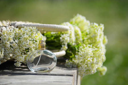 Transparent bottle of womens perfume on a wooden table on the background spring flower in a straw bag and green field.Eau de toilette with the scent of spring and summer flowers.Sprin gift for women.の写真素材