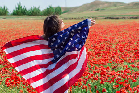 Girl in white clothes with an flag in her hands enjoys the wind and rays of the sun of a amazing red blooming poppy field.の写真素材