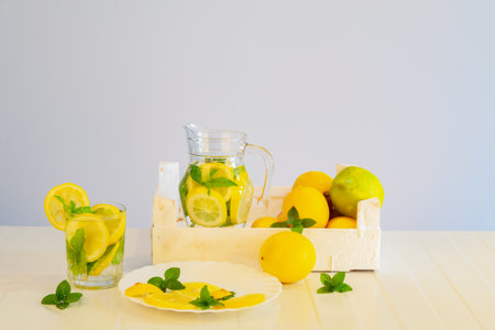Composition of fruits and cut pieces of lemon, mint leaves and sprigs and lemon drink in a jug, taken in natural light against a light background. Useful healthy fresh drink with mint and lemon.の写真素材