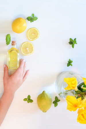 flat lay fruits lemon with women hand taken with natural light, preparing a healthy fresh drink lemon , mint and water.Helthy beverage with mentha and lemon.Hand holding bottle with lemon oilの写真素材