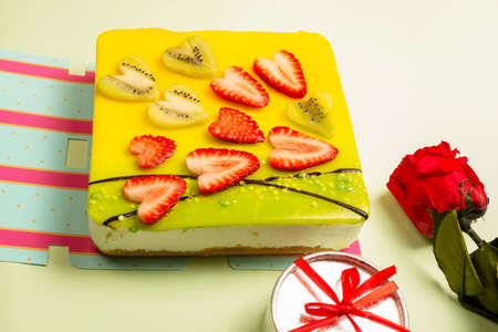 appetizing cake covered with icing, decorated with hearts of strawberries and kiwi pieces with a rose and a gift box on a light background,selective focus. Greeting card. Cake for Valentine's Dayの写真素材