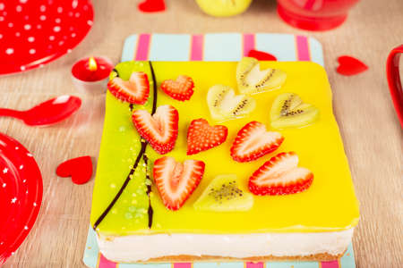 appetizing cake covered with icing, decorated with hearts from pieces of strawberries and kiwi on the festive table, close-up. Cake for Valentines Day, festive candyの写真素材