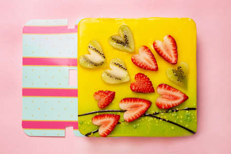 appetizing cake covered with icing, decorated with hearts from pieces of strawberries and kiwi on...