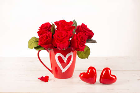 Red roses in a mug with a drawn heart on a table with decorative hearts. Festive concept, Valentines day card, Romantic home decor for Valentines Day,の写真素材