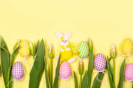 Fabric rabbit, souvenir eggs and flowers on a yellow background, copy space. Background for greeting...