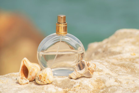 transparent spray bottle of womens perfume with shells close up on a stone against the backdrop of the sea in the sun. Presentation of womens perfumes in the sea environmentの写真素材