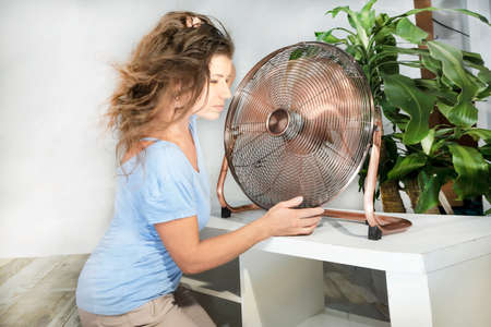 woman holding a fan with her eyes closed, enjoying the wind from the blades.の写真素材