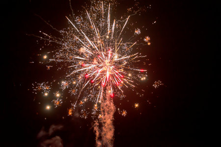 beautiful festive background of stars, splashes, sparks and bright lines of lights with smoke from a firework explosion with red color on a black sky background.の写真素材