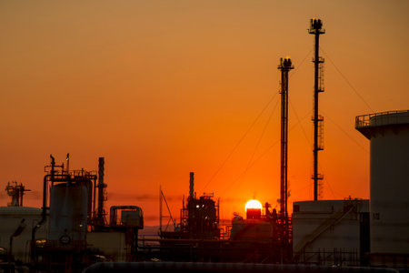 silhouettes of structures, pipes, oil storage tanks, pipelines of a petrochemical plant in the backlight of the sun at sunset and a sun disk.の写真素材