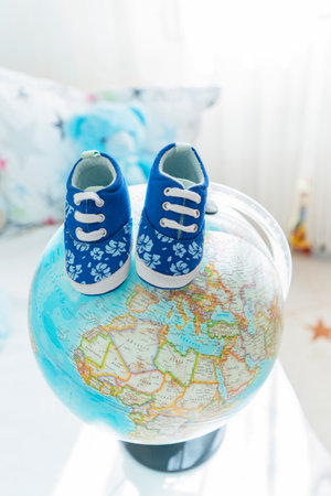 Little childrens shoes stand on a globe. The concept of traveling and entering the world of a small personの写真素材