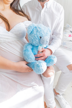 man hugs a pregnant woman with a teddy bear, close-up. Expecting a child, family happiness. Concept of expecting a child by a married coupleの写真素材