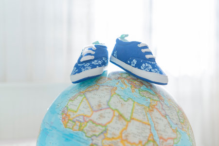 Little childrens shoes stand on a globe. The concept of traveling and entering the world of a small personの写真素材