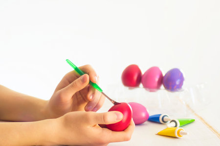 Easter egg coloring process with a brush of acrylic paints, hand action on a white table on a white background of the room.two hands paint eggs close-up with a bright paint brush.Handmade,hobbyの写真素材