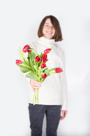 The guy holds out flowers.Tulips in the hands of a young man.Flower greetings.Man's hand with a bouquet of spring flowers.Man with tulips.Gift for mother,woman,girl and mother's day,March 8,birthday.の写真素材