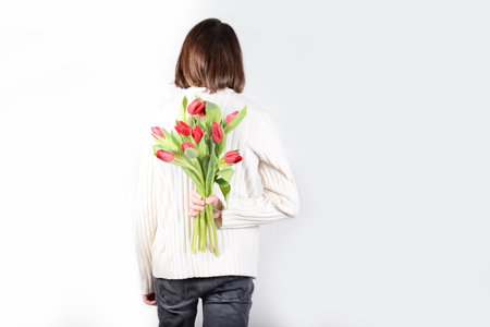 a man holds flowers behind his back. Tulips in the hands of a young man. Flower greetings for women...