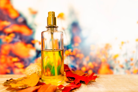 Perfume bottle on a wooden surface with orange and red fallen leaves against a background of beautiful blurred orange red and gray stains. Autumn concept for the presentation of gift accessoriesの写真素材