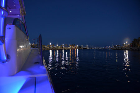 a gorgeous view from the side of a neon-lit yacht of the night sea with reflections from the illumination of the port. Night landscape view from the shore and the city embankment glowing with lightsの写真素材