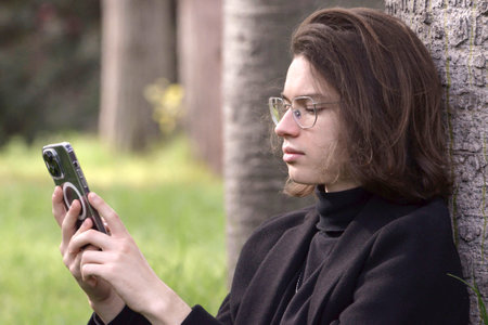 Student guy in glasses and business clothes,holding a cell phone dialing a number,looking at the screen.の写真素材