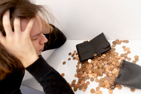 a young man with stressful emotions holds his head with his hands over a mountain of small coins with a wallet, a piggy bank bag. The concept of poverty, money crisis, low income,hopelessness, despairの写真素材