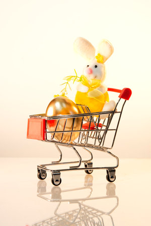 Shopping trolley with a golden egg and a toy hare, Easter bunny. Buying and increasing the price of colored eggs for Easter. Preparation for the holiday.の写真素材