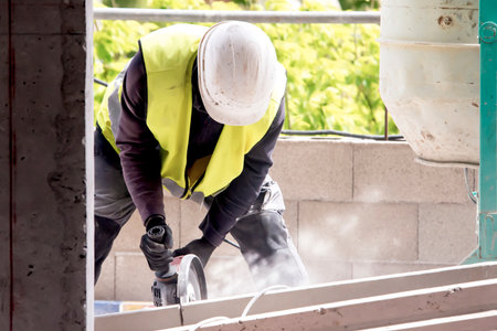 A worker in protective equipment works with a circular machine, cutting the structure, raising dust...